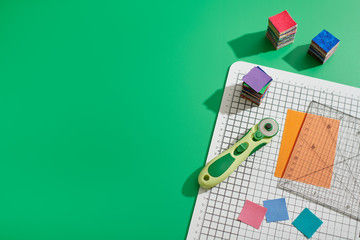 Rotary cutter, ruler, bright square pieces of fabric, stacks of bright fabric square pieces on...