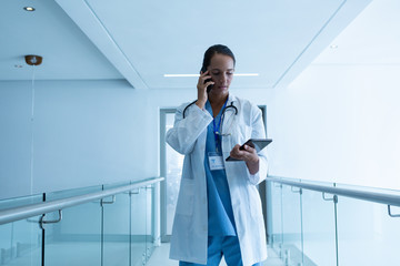 Female surgeon talking on mobile phone while using digital tablet at hospital