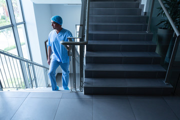Male surgeon looking through window while climbing up stairs of hospital