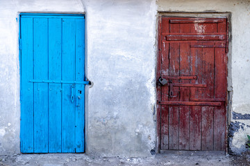 old wooden doors to poor homes. Colored wooden doors to the barn. Old colored doors with bolts. Peeling wall of the barn with a wooden door.