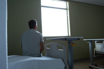 Thoughtful male patient sitting on bed in the ward