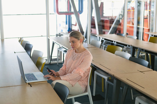 Female executive using laptop while holding mobile phone in the conference room
