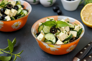 Healthy salad with cucumbers, feta and olives, with olive oil and greens, located in bowls against a dark background, horizontal photo