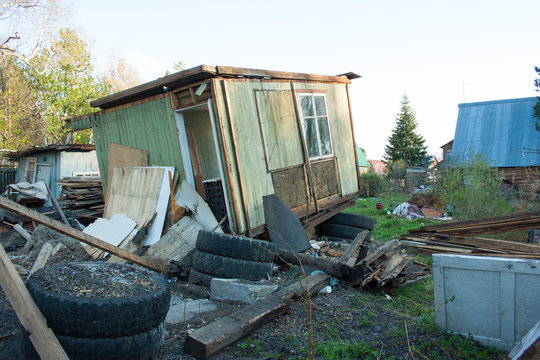 Completely ruined wooden house. Around different trash, tires, boards, pieces of plywood