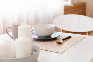 Cutlery, mug and plate and candles for decoration are on the kitchen table.