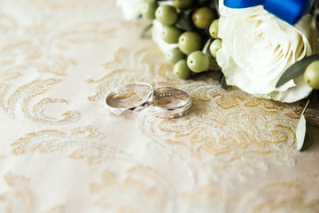 wedding rings lie on the fabric next to a bunch of flowers