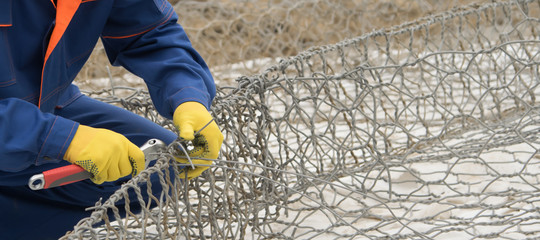 Fototapeta premium hands worker knit mesh for cells under the stones to improve the shore, close-up