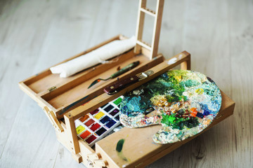Wooden folding suitcase artist with brushes, paint and palette. Background of a wooden floor