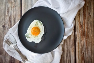 Fried eggs on a black round plate with greens on a brown wooden background