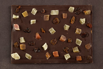 dark chocolate bar with candied fruits on brown background