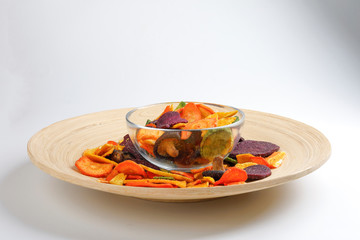 Healthy vegetable chips yellow sweet potato purple sweet potato carrot green radish green beans and shiitake mushrooms in glass bowl wooden plate