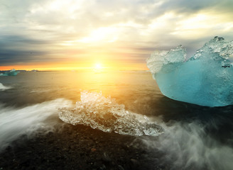 Emerald ice floes on a rocky volcanic beach at sunset. Glacial Lagoon. Iceland.Long exposure.