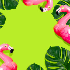 Creative summer beach concept. Inflatable pink mini flamingo and tropical leaf monstera on green background, pool float party. Flat lay copy space. Flamingo Trend Inflatable Toy. Summer background