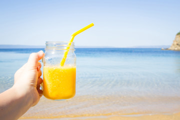 Fruit cocktail  in woman hand against tropical beach. Summer refreshment. Travel and vacation concept. Copy space