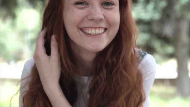 Red-haired emotional girl making faces. Freckled ginger girl in park close-up. Young red-headed woman on blurred background show tongue.