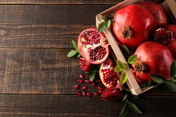 Ripe tasty red pomegranate fruit with leaves in a wooden box on a brown wooden table. top view