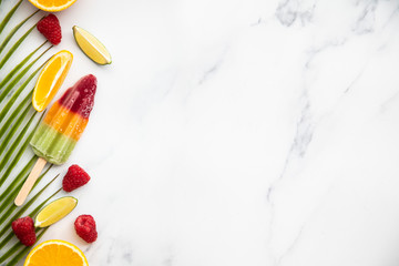 Summer ice lollies with fruit and a tropical palm leaf
