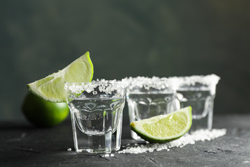 Tequila shots with salt and lime slices on black background