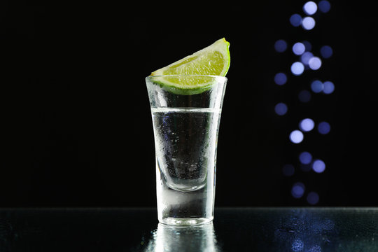 Tequila shot with lime against black background with blurred lights