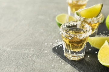 Tequila shots with salt and lime slices on grey background