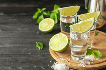 Tequila shots with lime slices, salt and mint on wooden background