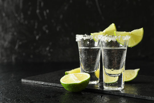 Tequila shots with salt and lime slices on black wet background