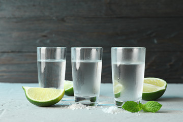 Tequila shots, salt, lime slices and mint on table against wooden background