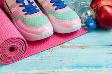 Fototapeta na wymiar Pink yoga mat, sport shoes, bottle of water and apples on blue wooden background. Healthy lifestyle, yoga, sport concept. Trendy female sport equipment. Copy space
