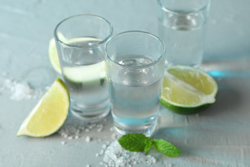 Tequila shots, salt, lime slices and mint on white cement background