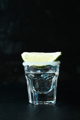 Tequila shot with lime and salt against black background with blue light