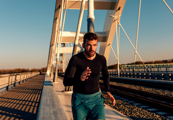 A handsome man running at bridge during sunset.