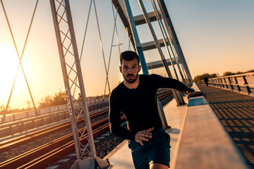 A handsome man running at bridge during sunset.