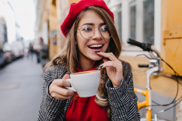Close-up photo of enchanting lady in tweed coat holding cup of coffee and laughing on blur urban...