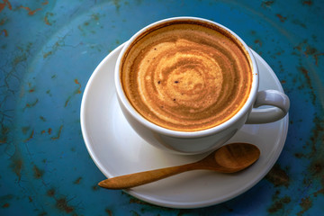 A hot coffee in white cup serving on blue rustic table 