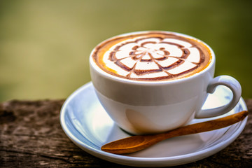 a cup of hot coffee with latte art, serving on wooden table in day light
