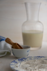 View of ingredients for pastry, flour with milk bottle and dishcloth on white wooden background