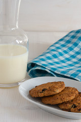 Top view of cookies with milk bottle and blue kitchen towel on white wooden background