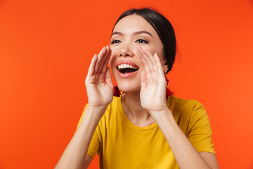 Excited happy young woman posing isolated over orange wall background screaming talking.