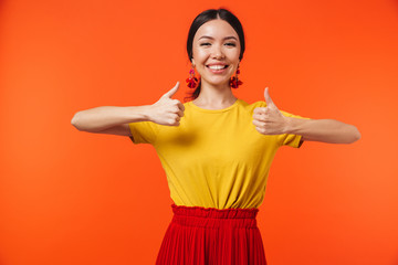 Excited happy young woman posing isolated over orange wall background make thumbs up gesture.