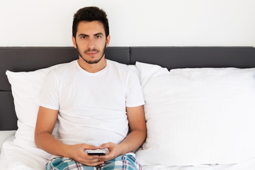 Young handsome man sitting on the bed. He uses a mobile phone. The problem of dependence on mobile social networks.