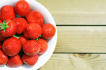 Bowl of fresh ripe Strawberries in a white fruit bowl on a rustic picnic table.