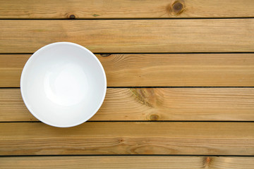 Empty white bowl on a wooden table - directly above with copy space.