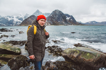 Obraz premium Traveller professional photographer taking nature photo of landscape. Wearing a yellow backpack wearing a red hat standing on rocks against the background of the sea and the mountains