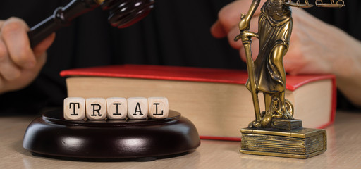 Word TRIAL composed of wooden dices. Wooden gavel and statue of Themis in the background.