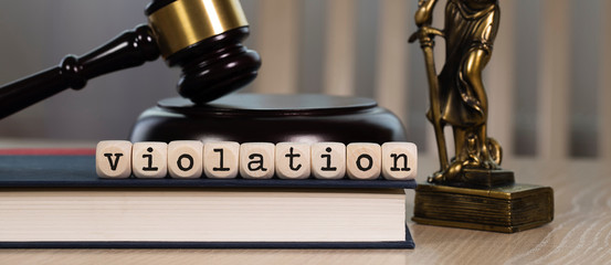 Word VIOLATION composed of wooden dices. Wooden gavel and statue of Themis in the background.
