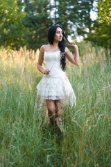 Young pretty brunette woman in white wedding dress, walking in the forest and smiling