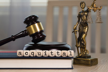 Word  ACQUITTAL composed of wooden dices. Wooden gavel and statue of Themis in the background.