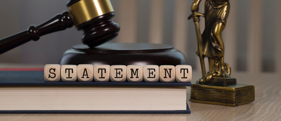 Word STATEMENT composed of wooden dices. Wooden gavel and statue of Themis in the background.
