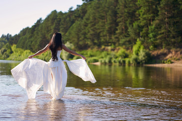 Fototapeta na wymiar Young pretty brunette woman in white wedding dress, walking on the river