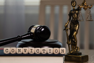Word CONVICTION composed of wooden dices. Wooden gavel and statue of Themis in the background.